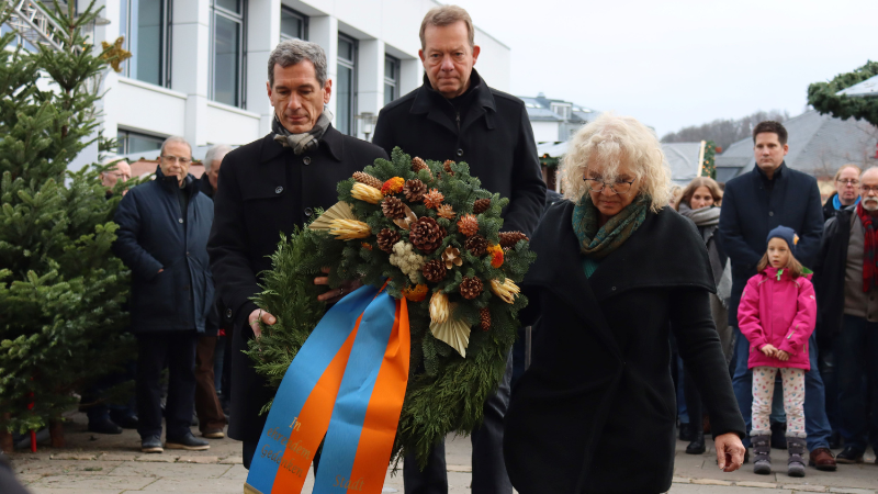 Bürgermeister Steffen Mues (mitte) mit seinen Stellvertretern Angela Jung (rechts) und Jens Kamieth (links) tragen einen mit Stadtfarben geschmückten Kranz zur Gedenkstätte im Dicken Turm. (Foto: Stadt Siegen)