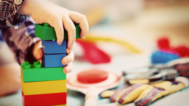 Symbolfoto: Kindertagespflege. Zu sehen sind Kinderhände, die Legosteine übereinander stapeln. Im Hintergrund sind weiter Spielzeuge zu erkennen(Foto: www.pixabay.com/Esi Grünhagen)