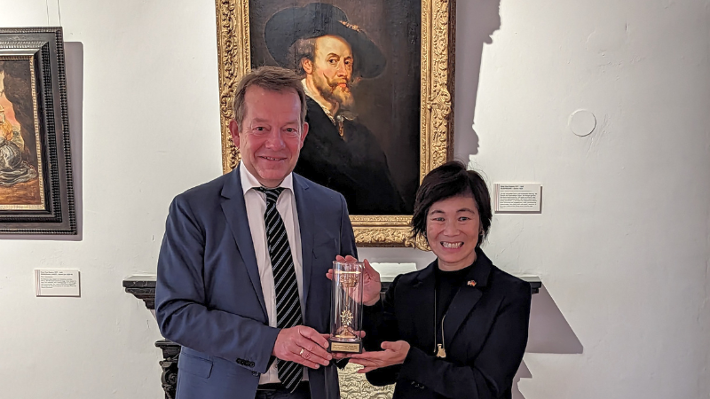 Bürgermeister Steffen Mues überreicht der Generalkonsulin Pauline Kao im Siegerlandmuseum das goldene Krönchen der Stadt Siegen. Im Hintergrund ist ein Portrait des Malers Peter Paul Rubens zu sehen.